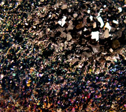 Synthetic silicon carbide crystal aggregate: iridescent twinned crystals in foreground with untwinned tabular crystals in background. They have a metallic lustre and are razor-sharp.