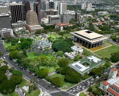 The Capitol District (foreground) incorporates historic buildings dating back to the monarchy of . The state capitol is the large building at middle right with columns set into a surrounding reflecting pool. The intersection at the bottom is King and Punchbowl streets, with the State library (green and white roof) and Honolulu city hall (Honolulu Hale; red tile roof) across Punchbowl from each other.  is just left of center in this photograph. The buildings of downtown Honolulu backdrop the Capitol District