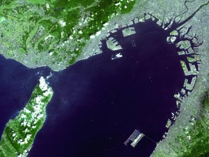 Satellite photo of Kansai Airport (lower-right island) in Osaka Bay.  is being built on the unfinished island near the middle of the photo. Central Osaka is in the upper-right corner.