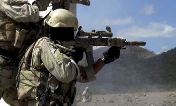 A US Army SF operator takes aim with his desert camouflage painted SPR. An Insight Technologies AN/PEQ-2A Target Pointer/Illuminator Aiming Light (TIPAL) is mounted on the right of the rifle's handguards. A standard M4 telescoping stock is used on this one.
