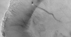 A dust devil on , photographed by . The long dark streak is formed by a moving swirling column of Martian atmosphere. The dust devil itself (the black spot) is climbing the crater wall. The streaks on the right are sand dunes on the crater floor.