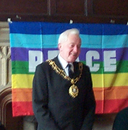 Councillor Patrick (Pat) John Stannard, Lord Mayor of Oxford (2004) standing in front of a peace flag.