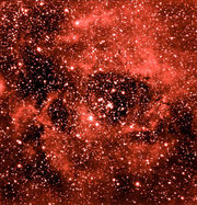 Embedded in the center of the Rosette Nebula is an open cluster. The blue stars in this cluster, labelled NGC 2244, emit ultraviolet light that knocks electrons away from hydrogen atoms. When the electrons fall back, they emit the red light seen here. The Rosette Nebula is about 100 light-years across.