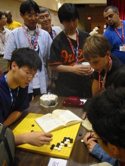 Three Japanese professional Go players observe some younger amateurs as they dissect a life and death problem in the corner of the board, at the  in , .