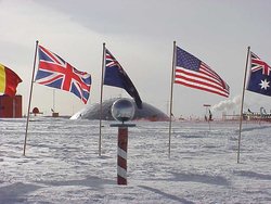 The ceremonial South Pole.  Flags of the  signatories are arrayed around it, and the Pole Station's old dome is in the background.